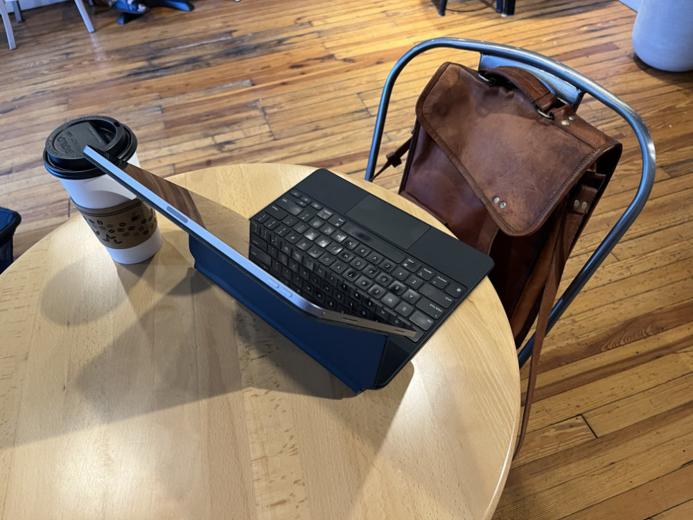 A leather bag sitting in front of an iPad and a cup of coffee.